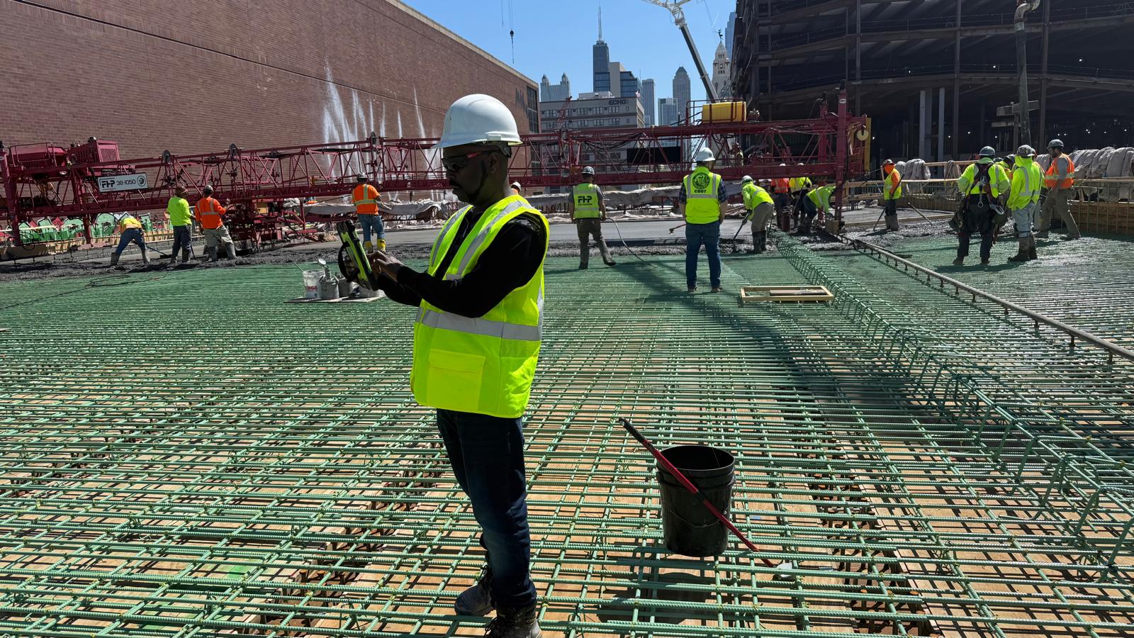 CHI-UG engineer in hard hat and safety vest on a reinforced concrete deck with cranes and city skyline