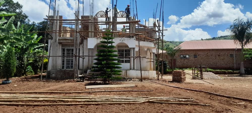 Two-storey residential building under construction with workers and scaffolding in Uganda.